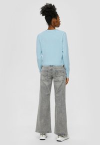 Jasnoniebieski sweter z dzianiny z długimi rękawami, zestawiony z szarymi spodniami w szerokiej nogawce i białymi trampkami, widok z tyłu.