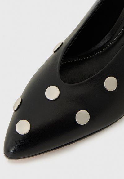Črne usnjene čevlje s pointe točko, ki imajo na zgornji površini srebrne okrogle žebljiče, z gladko teksturo in kontrastnim belim šivom.