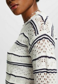 Pull en maille crème avec des rayures bleu marine. Comprend un motif en dentelle, une maille texturée et un col rond. Tissu léger et respirant.