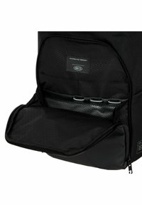Interior de mochila negra de nylon con un patrón hexagonal, una etiqueta y bolsillos organizadores con detalles de malla y cierre de cremallera.