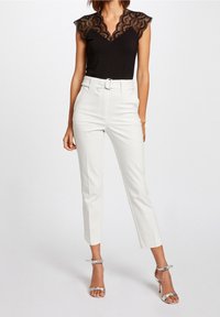 Czarny top z koronkowymi rękawami i dekoltem w serek, zestawiony z białymi spodniami o wysokim stanie z paskiem. Srebrne sandały na obcasie.