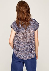 Blouse à manches courtes florale en marine, en tissu léger et transparent avec un imprimé floral rose et blanc, ourlet arrondi et détails froncés.