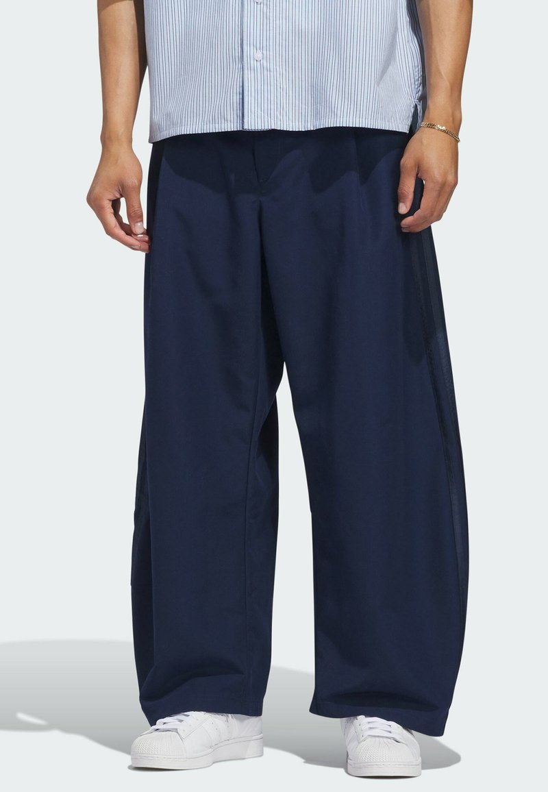 Persona que lleva pantalones azul marino holgados, zapatillas blancas y una camisa de rayas azul claro.