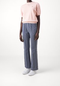 Jasnoróżowa bluza z krótkim rękawem, niebieskie rozszerzane spodnie w wzory z bocznymi paskami oraz białe trampki. Miękka tekstura, luźny krój, geometryczny wzór.