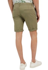 Pantalones cortos verde oliva confeccionados en una tela ligera, con dobladillos enrollados y bolsillos traseros, combinados con zapatillas blancas.