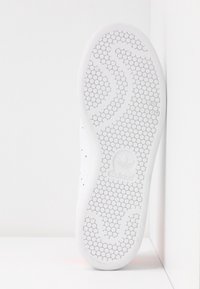 White sneaker sole with a hexagonal pattern, smooth texture, and branding detail. Side features perforations for breathability.