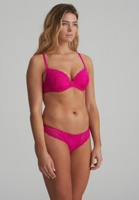 Reggiseno in pizzo rosa con bordo scallop e supporto con ferretto, abbinato a slip in pizzo coordinati con un accento decorativo al centro.