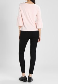 Ljusrosa topp med trumpetärmar, kombinerad med svarta slim-fit byxor och svarta skor. Slät tygkvalitet, figurnära design och skräddarsydd look.