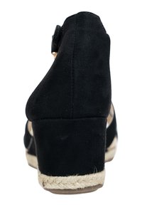 Zapato de tacón cuña de ante negro con una base envuelta en yute y un pequeño detalle de hebilla en la parte trasera. Superficie texturizada, forma redondeada.