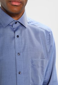Light blue button-up shirt with a textured pattern, pointed collar, and a single chest pocket featuring a small logo.