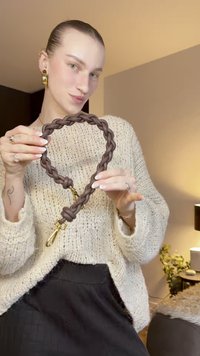 Lesă maro împletită, realizată din material moale, cu accesorii metalice aurii. Textura pare netedă și flexibilă, evidențiind o țesătură complexă.