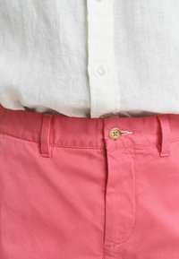 Roze katoenen shorts met een knoopsluiting en riemlussen, gedragen met een witte linnen blouse met een knoopsluiting aan de voorkant. Katoen met een gladde textuur is zichtbaar.