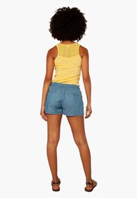Keltainen hihaton paita, jossa on brodeerattu selkäosa, yhdistetty sinisiin shortseihin, joissa on joustovyötärö ja takataskut. Sandalet täydentävät asun.