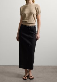 Lichtbeige, gebreide top met korte mouwen en subtiele patronen, gecombineerd met een lange zwarte rok met een tailleband en platte zwarte sandalen.