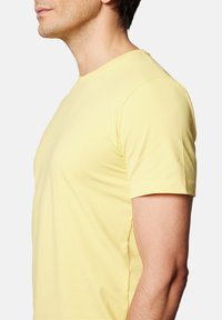Żółta bawełniana koszulka z krótkim rękawem, klasyczny okrągły dekolt, gładka tekstura i dopasowany krój, pokazana z boku.