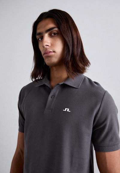 Graues Polo-Shirt aus strukturiertem Stoff mit einer Knopfleiste mit drei Knöpfen und einem weißen Logo auf der linken Brust. Kurze Ärmel.