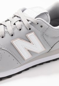 Graue Sportschuhe mit einem strukturierten Mesh-Obermaterial, gummierter Sohle und prominentem weißen "N"-Logo. Verfügt über graue Schnürsenkel und einen gepolsterten Kragen.