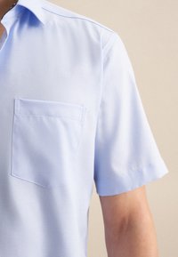 Camicia a maniche corte in tessuto azzurro chiaro con colletto all'italiana, taschino frontale singolo e dettagli di cucitura sottili lungo il colletto.