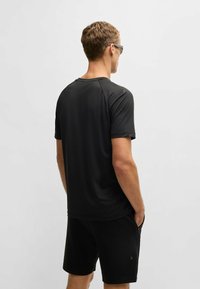 Svart tränings-T-shirt i lätt tyg, med korta ärmar och en avslappnad passform. Bärs med svarta shorts, utan synliga mönster.