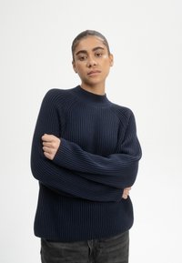 Nachtschwarzer gerippter Pullover mit hohem Kragen, weiten Ärmeln und einem entspannten Schnitt. Strukturiertes Strickmaterial mit sichtbaren vertikalen Linien.