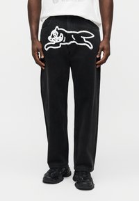 Μαύρο παντελόνι τζιν με λευκό κεντητό σχέδιο ενός άλτη ζώου στο πίσω μέρος. Χαλαρή εφαρμογή με τσέπες κανονικού μεγέθους και θηλιές για ζώνη.