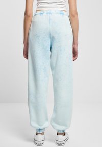 Svjetloplave trenirke s izbljeđenim tie-dye uzorkom, elastičnim pojasom i suženim gležnjevima. Uparene s bijelim tenisicama.