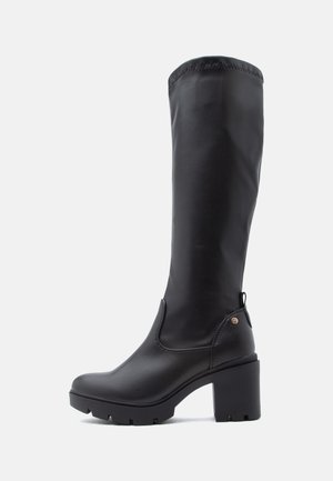 Botte haute en cuir noir avec talon bloc épais et semelle robuste, avec une petite languette à l’arrière et des détails de couture minimaux.