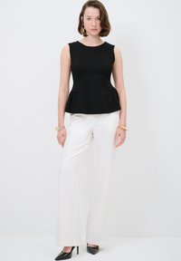 Schwarzes Peplum-Top mit Rundhalsausschnitt, kombiniert mit weißen weit geschnittenen Hosen. Das Outfit zeichnet sich durch minimale Akzente und ein schlankes Design aus.