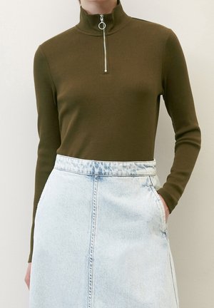 Olivgrünes, geripptes Langarmoberteil mit einem hohen Kragen und silbernem Reißverschluss, kombiniert mit einem hellblauen Jeansrock mit einer vorderen Naht.