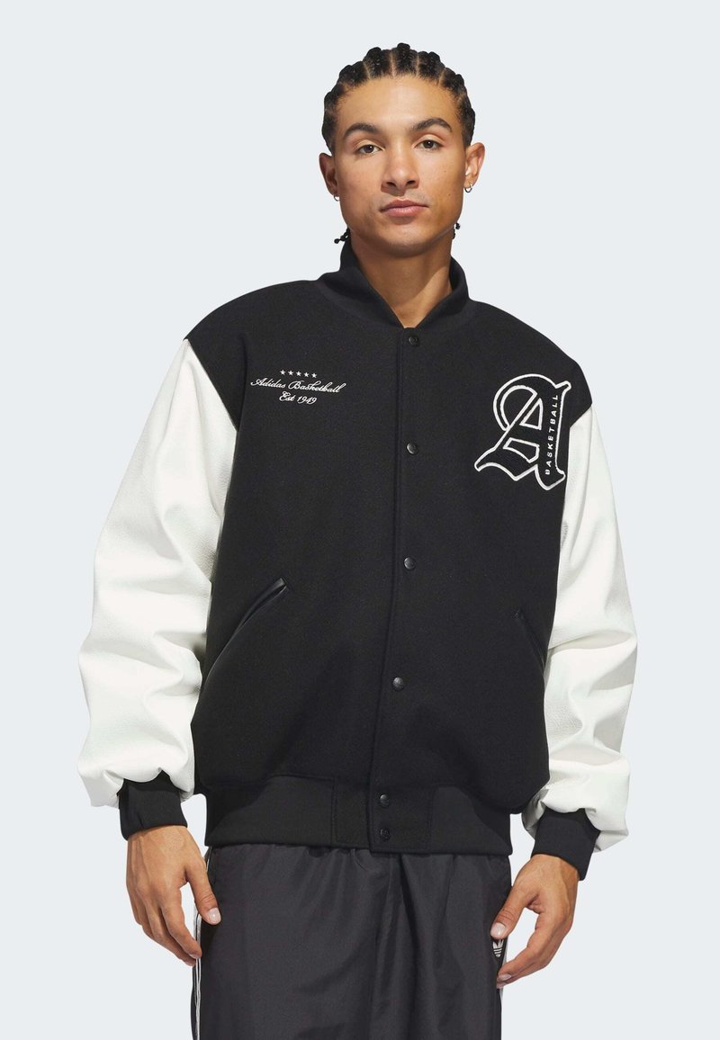 Black and white varsity jacket with a wool body, leather sleeves, embroidered logo, snap buttons, and side pockets.