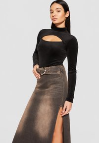 Long black mock neck top with a cutout, paired with a high-waisted dark denim skirt featuring a side slit and a round silver buckle belt.