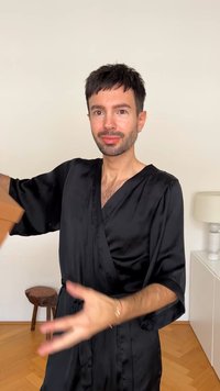 Melnas satīna halāts ar platām piedurknēm un sasietu jostas vietu. Materiālam ir gluda tekstūra. Fons ietver gaišas krāsas mēbeles.