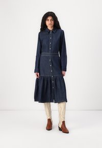 Robe en denim à manches longues avec un devant à boutons, jupe à volants, poche poitrine et ceinture détachable ; présente des coutures contrastées et une coupe décontractée.