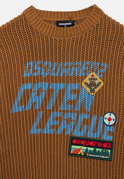 Pull en maille marron avec texte bleu "CANTEEN LEAGUE", écusson jaune "CAMP 95", patch boussole et patch coloré sur le thème du camping avec l'inscription "ADVENTURE IS CALLING."