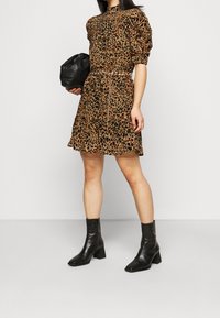 Nahkakuosiset mekko, jossa on puffihihat, korkea kaula-aukko ja röyhelöhelma. Yhdistetty mustiin nilkkureihin ja mustaan laukkuun.