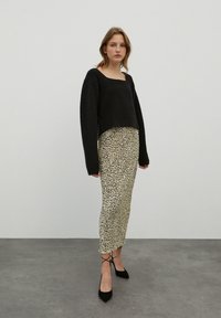 Zwarte cropped trui met een vierkante hals, gecombineerd met een middellange rok met panterprint en zwarte puntige hakken. Overal een gladde textuur.