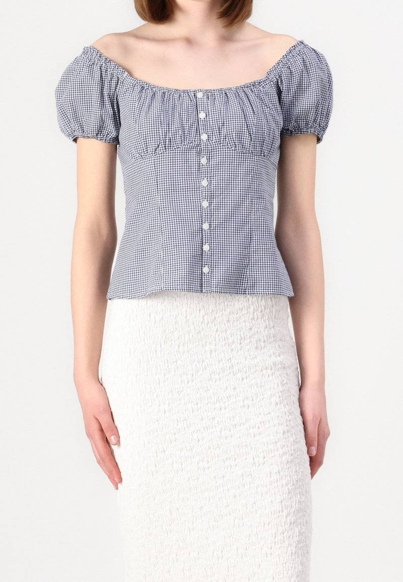 Blusa scollata in navy e tessuto a quadri bianchi. Maniche a sbuffo, corpino aderente e abbottonatura frontale bianca.