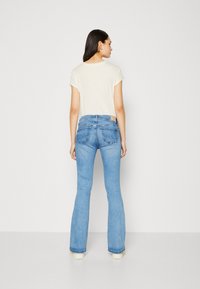 Ljusfärgad t-shirt i kombination med figurnära blå utsvängda jeans med en subtil blekning, två bakfickor och en märkesläderlapp.