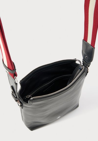 Black leather crossbody bag with red and white striped adjustable shoulder strap, open top zipper, and inner zippered compartment.