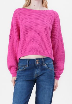 Woman wearing bright pink textured knit sweater with balloon sleeves and blue high-waisted jeans with double button closure.