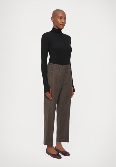 Pullover negru cu maneci lungi și guler tip tutore, pantaloni maro texturat cu talie înaltă și balerini burgundy. Pantalonii au un elastic în talie și croi dreapt.