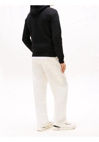 Black hooded sweatshirt with a fitted design, worn with white cargo pants featuring side pockets. Shoes are white with black accents.