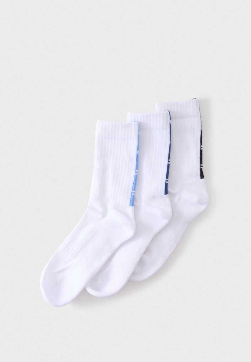 Trois paires de chaussettes blanches montantes avec des bandes colorées le long des côtés en bleu clair, bleu foncé et noir, posées en chevauchement sur un fond clair.