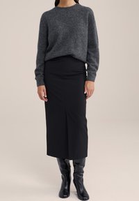 Grå stickad tröja, figurnära svart blyertskjol, knähöga svarta stövlar. Tröjan har ribbade ärmslut; kjolen har en frontslitsdetalj.