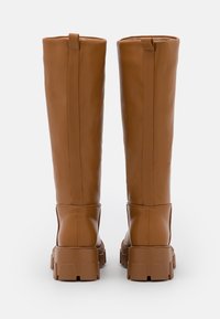 Wysokie brązowe skórzane botki z grubymi gumowymi podeszwami, widocznymi pętelkami z tyłu oraz pionowymi szwami wzdłuż tylnego panela.