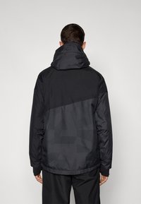 Sort hættejakke med et struktureret design, der har kontrasterende matte og blanke sektioner, elastiske manchetter og en høj krave.