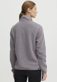 Giacca in fleece grigio chiaro con colletto alto. Tessuto morbido, maniche lunghe e taglio dritto. Piccolo logo sul lato sinistro in basso.