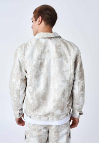 Lysfarvet denimjakke med et tekstureret, abstrakt mønster i nuancer af beige og hvid. Har standardkrave og knapper.
