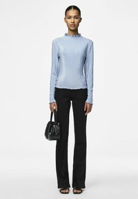 Maglietta azzurra a maniche lunghe con scollatura arricciata, abbinata a pantaloni neri a campana. La modella tiene una piccola borsa nera.