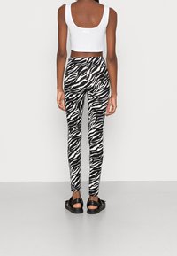 Leggings con stampa zebra bianco e nero dal design aderente, abbinati a un top corto bianco e sandali neri.